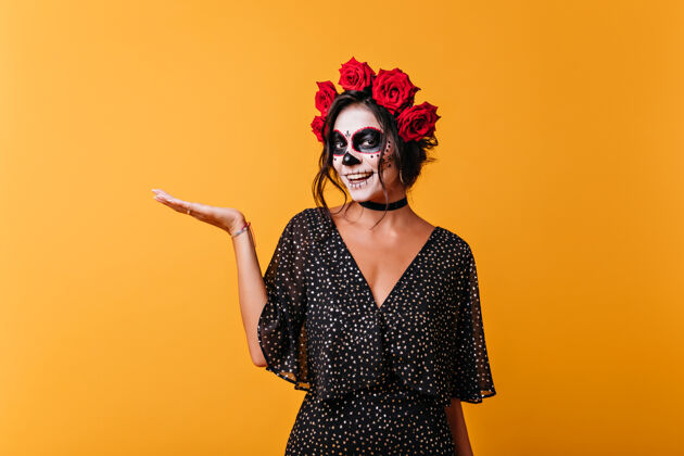 油漆黄色背景上摆着笑脸的僵尸女士穿着墨西哥万圣节服装的漂亮女模特对着镜头微笑女人幽灵女孩