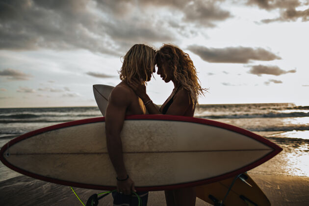 情侣肌肉男和他苗条的女孩互相欣赏情侣们在冲浪板前摆姿势浪漫男人海洋