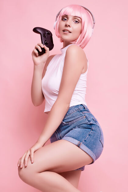 情感美丽快乐的游戏女孩与粉红色头发的肖像玩游戏机上五颜六色的操纵杆在工作室玩家在线操纵杆