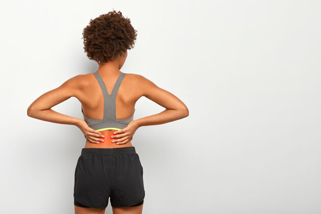 发型留着非洲式发型的运动型女人用双手触摸腰部 感觉脊椎疼痛 显示发炎部位 穿灰色上衣疾病姿势脊柱