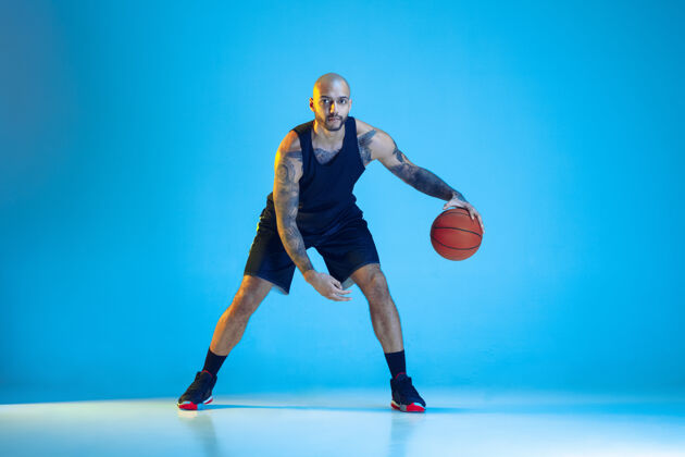 射击年轻的篮球队员穿着运动服训练 在运动中练习 运动在霓虹灯下隔离在蓝色的墙上运动的概念 运动 活力和活力 健康的生活方式运动员比赛年轻