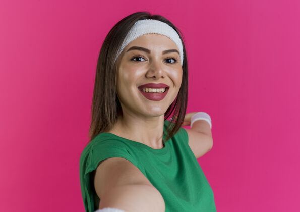 穿戴着头带和腕带的年轻运动女性的特写镜头看着并伸出双手运动粉色头带