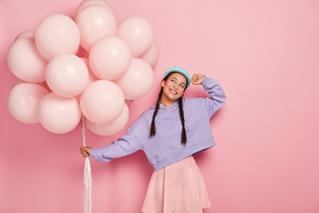 快乐快乐的亚洲年轻女子 梳着两条辫子 梦想着美好的节日 带着一堆气球 想象着美丽的庆祝时刻 孤立在粉红色的墙上束室内模特
