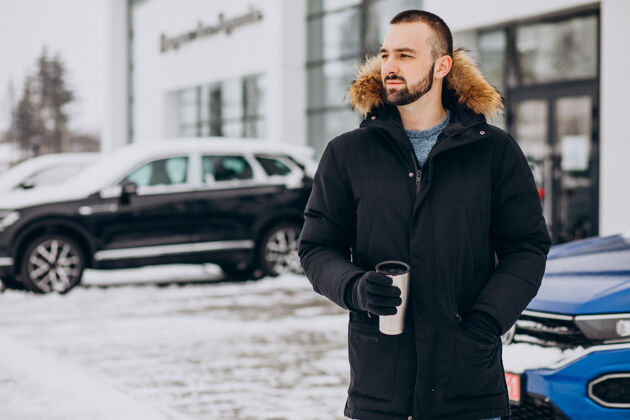 卡住穿着暖和夹克的帅哥站在被雪覆盖的汽车旁喝着咖啡旅行旅游冰冻