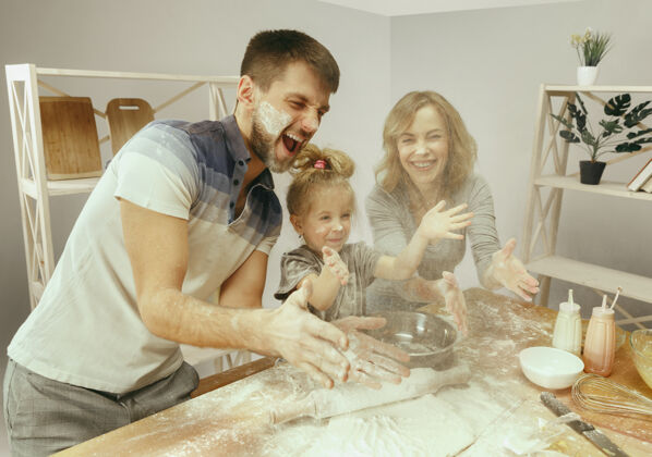 食物可爱的小女孩和她美丽的父母在家里的厨房里为蛋糕准备面团孩子周末积极