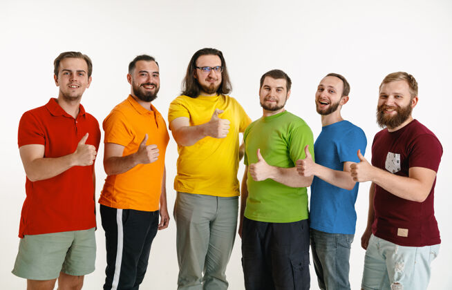 同性恋年轻人穿着隔离在白色墙壁上的lgbt旗帜颜色高加索男模穿着红 橙 黄 绿 蓝 紫的衬衫lgbt骄傲 人权和选择理念积极男人爱