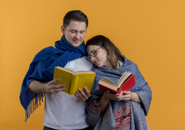 夫妻一对年轻夫妇拿着毛毯 抱着书 快乐而积极地微笑着 站在橙色的墙上年轻毯子女人