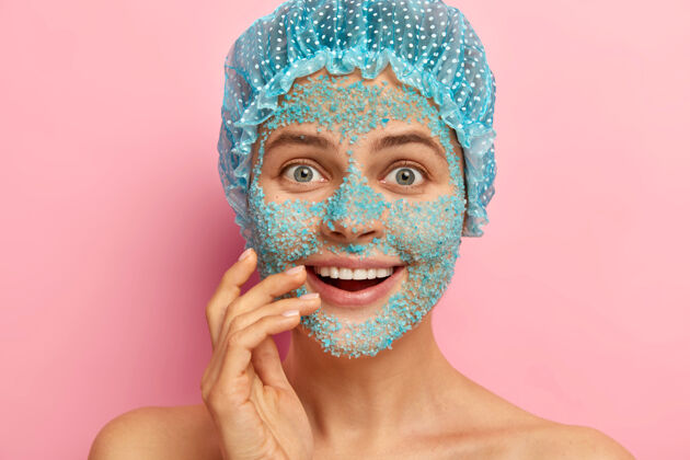 头像一脸幸福的惊喜女人 用海盐蓝色颗粒遮住脸 从毛孔和痤疮上剥皮 洗澡时戴上防护帽裸露纯洁人