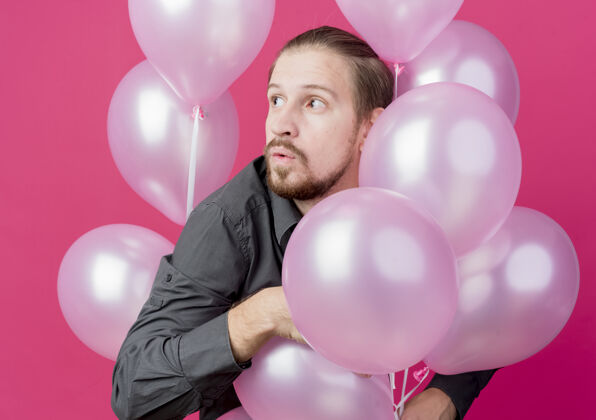 束年轻人正在庆祝生日聚会 一群气球站在粉红色的墙上 惊讶地看着旁边站男人一边