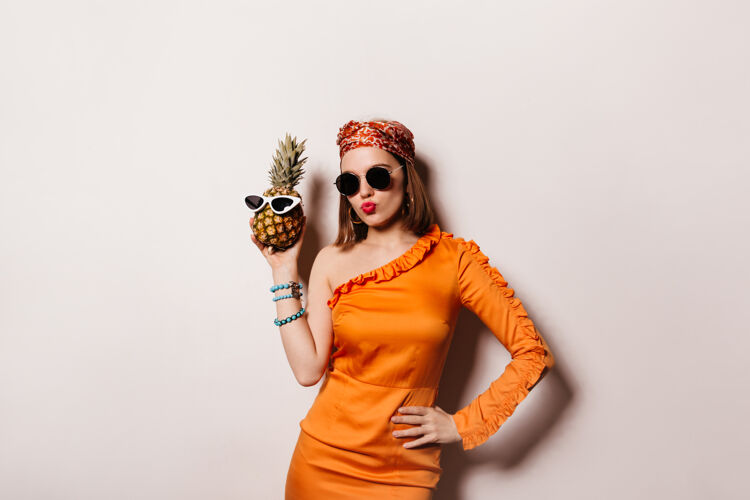女士美丽的短发女人戴着太阳镜 穿着时髦的橙色连衣裙 戴着菠萝眼镜水果好健康