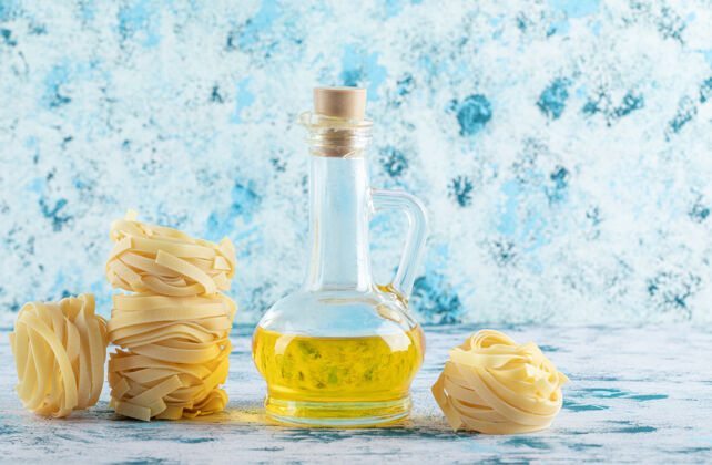 生的一堆塔格利亚特尔巢穴和一杯橄榄油在蓝色上烹饪干的意大利菜
