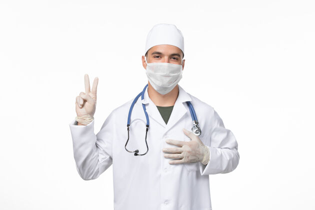 冠状病毒正面图：男医生穿着医疗服 戴着口罩 因为有冠状病毒-在光桌上的疾病病毒-冠状病毒-疾病套装听诊器冠状病毒预防
