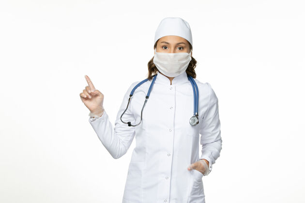 专业正面图：穿着白色医疗服 戴着白色面罩的女医生在淡白色的墙壁上吃潘多米病毒病药灯光制服护士