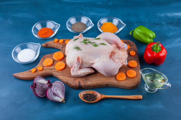 料理蔬菜 香料 油 勺子和生的整只鸡放在蓝色表面的砧板上配料生的生的
