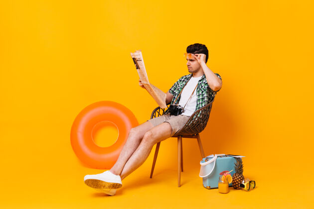 衣服一个穿着夏装的男人摘下眼镜 看报纸在橙色的空间里 他带着手提箱和橡胶圈的肖像椅子白色t恤鸡尾酒