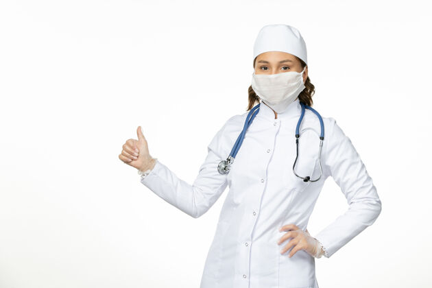 穿戴前视女医生身穿白色医疗服戴口罩因冠状病毒在浅白桌面大流行病毒隔离居家冠状病毒大流行