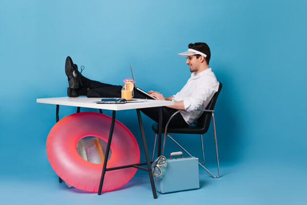 休息戴着帽子的家伙拿着笔记本电脑 两腿搁在桌子上坐着手提箱和充气圈的空隙衬托着男人的肖像充气圈现代潜水面具