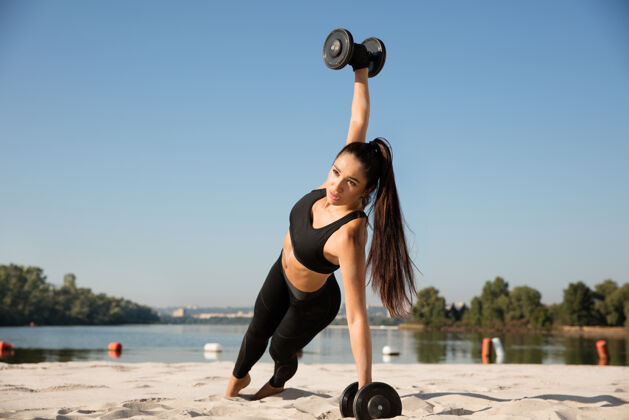 沙滩年轻健康的女子在沙滩上练习上身举重健康运动肌肉