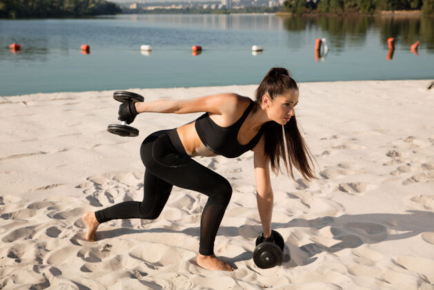 日落年轻健康的女人在沙滩上举重蹲着强壮身体单独