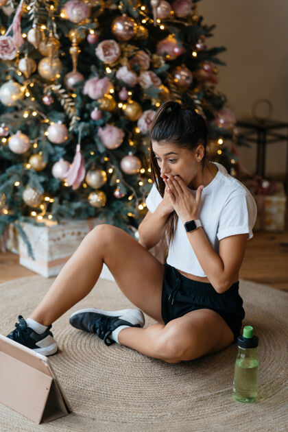 地板快乐的女人与家人或朋友视频通话年轻的女人在家里装饰好的圣诞树旁使用数字平板电脑平板电脑树视频通话