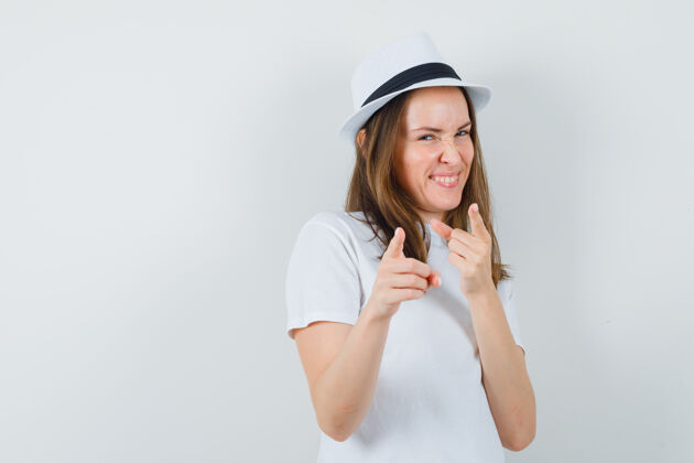 漂亮年轻女孩指着白色t恤 戴着帽子 看起来很活泼 正对着窗外快乐年轻帽子