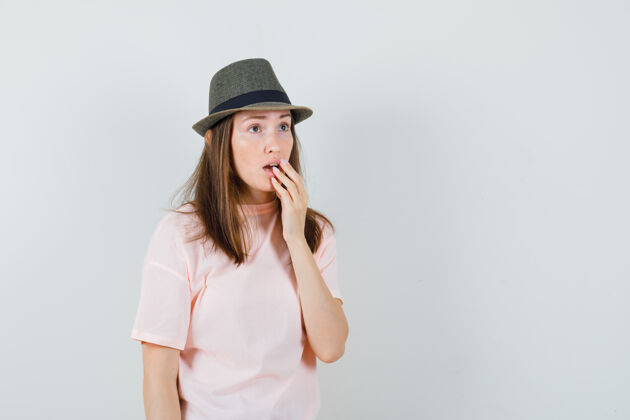 微笑身穿粉色t恤的年轻女性 戴着帽子 手放在张开的嘴上 神情好奇 前视图年轻开放帽子
