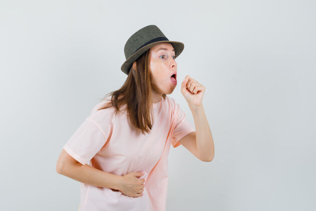 时尚患有咳嗽的年轻女性穿着粉色t恤 戴着帽子 看上去很不舒服 正前方视图积极帽子休闲