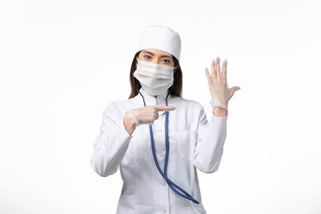 面罩正面图：女医生穿着白色无菌医疗服 戴着口罩 因为柯维德-在白色办公桌上展示她的手疾病柯维德-大流行病毒疾病大流行医疗套装