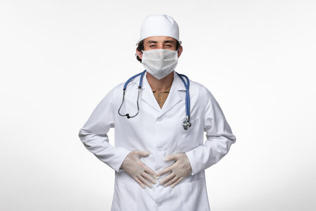 视图正面图：男医生穿着医疗服 戴着口罩以防病毒感染——患有胃痛的白墙病病毒——病毒感染——大流行实验室外套疼痛医疗