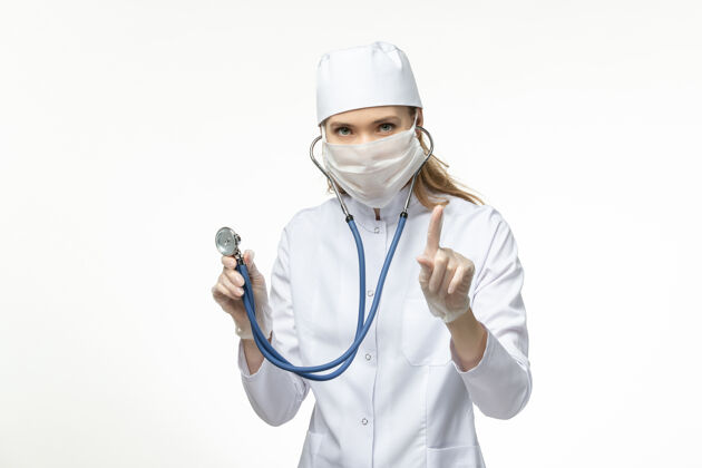 医疗器械正面图：穿着白色医疗服和面罩的女医生 在白色办公桌上防止冠状病毒感染视图大流行女性