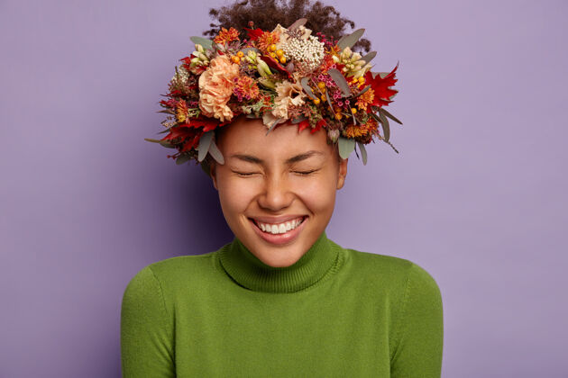 紫色可爱的非洲女人头像欢笑着戴着手工制作的秋天花环 笑容灿烂 穿着绿色高领毛衣微笑秋天非洲