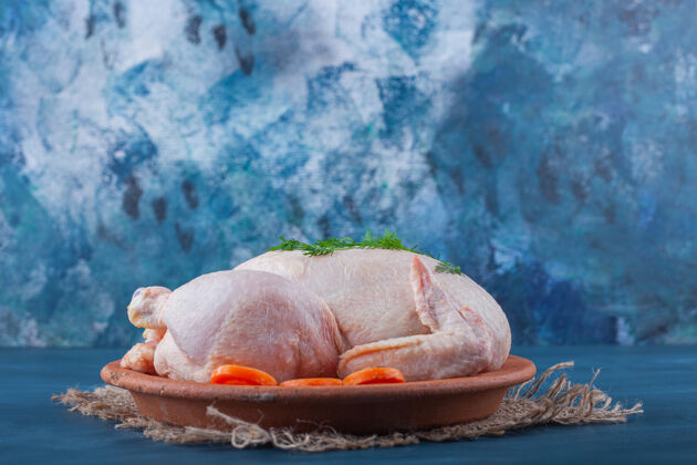 料理把整只鸡和切成片的胡萝卜放在盘子里 放在蓝色表面的粗麻布餐巾上开胃菜禽类美味