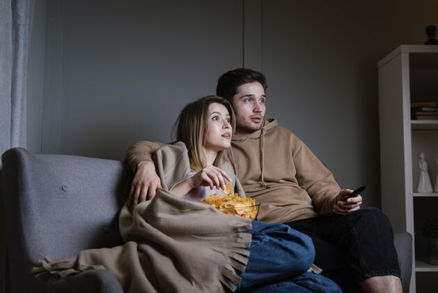 电视遥控器夫妻俩在沙发上看电视吃薯片男人看电视夫妇
