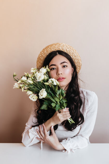 女性时尚的亚洲女人戴着草帽拿着白色的桔梗可爱的卷发女人的正面图 米色背景上有花束情感无忧无虑日本