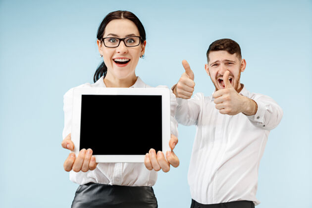 表演惊讶的商人和女人在蓝色的空间微笑 并显示笔记本电脑或平板电脑的空屏幕空虚胜利男性