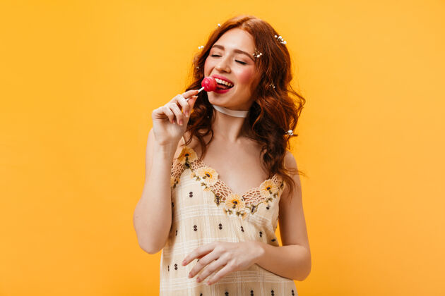 化妆品美丽的红发女子在格子夏季上衣舔棒棒糖与喜悦 摆出孤立的背景眼睛肖像棒棒糖
