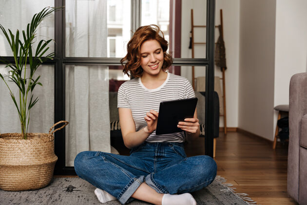 互联网穿着舒适衣服的年轻女子微笑着看着平板电脑 在客厅里摆姿势坐着沙发年轻