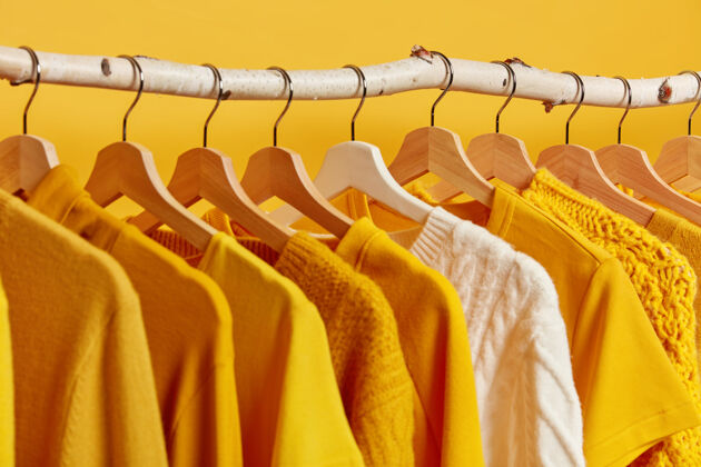 服装一排时髦的衣服挂在黄色背景的木架上白色针织毛衣在冬天的服装收藏中脱颖而出室内明亮各种
