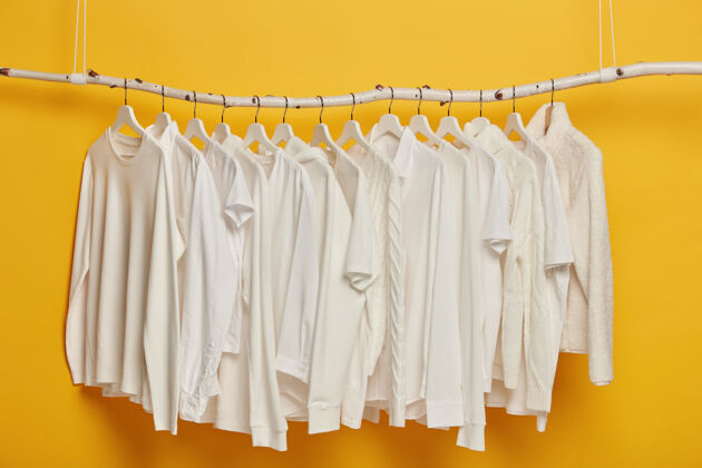 休闲一组白色的便衣挂在衣架或横杆上简约的概念黄色背景下的女性服装毛衣悬挂选择