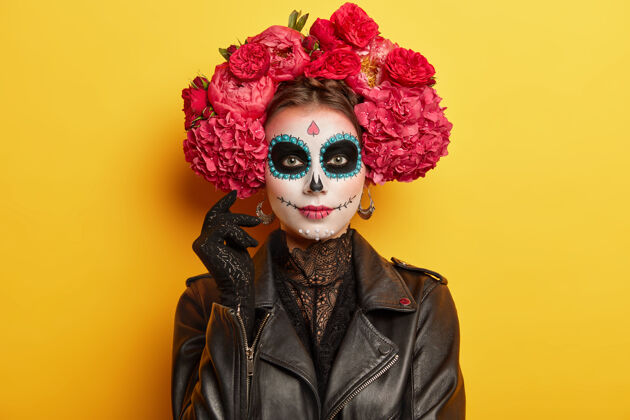 花墨西哥节日的女参与者有专业的妆容 黑眼睛戴着红牡丹花环装扮成精神模特在室内生动的墙上幽灵室内夹克