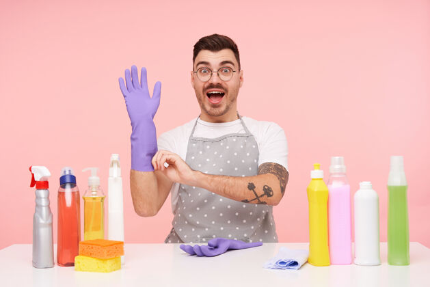 眼镜激动的年轻漂亮纹身黑发男子举起手在橡胶手套男士洗涤剂制服