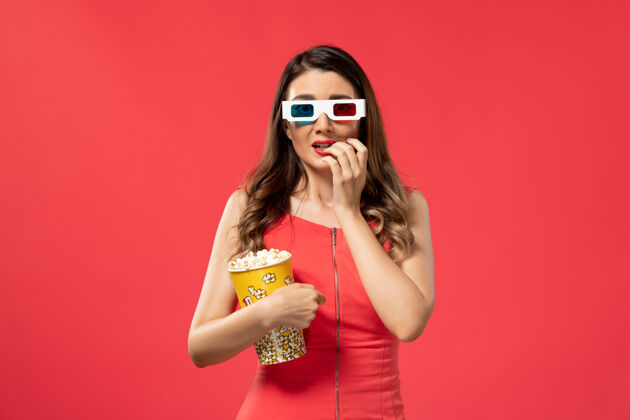 漂亮正面图年轻女性手持爆米花包戴着d墨镜在红色表面爆米花电影举行
