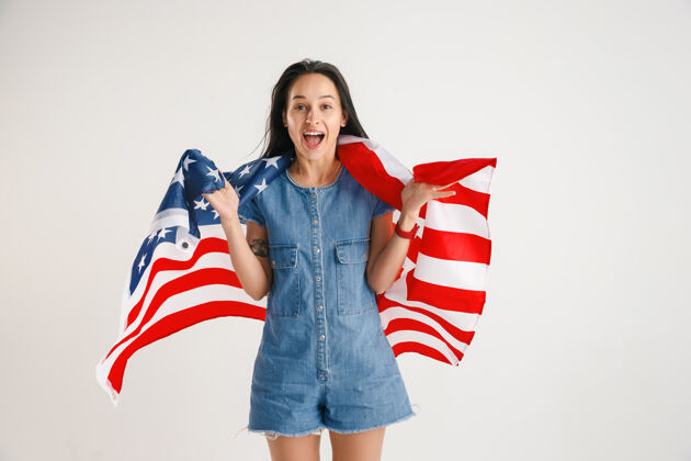 美国庆祝独立日星条旗白色工作室墙上挂着美国国旗的年轻女子看起来像个疯狂的快乐和自豪的爱国主义者女人明星立场