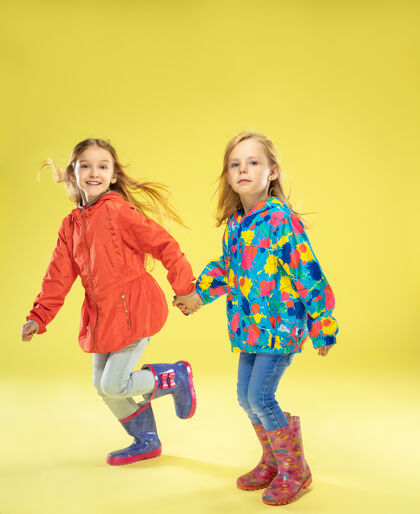 休闲黄色的画室墙上 一个穿着雨衣 手牵着手 奔跑着 玩得很开心的时髦女孩的完整肖像明亮童年春天