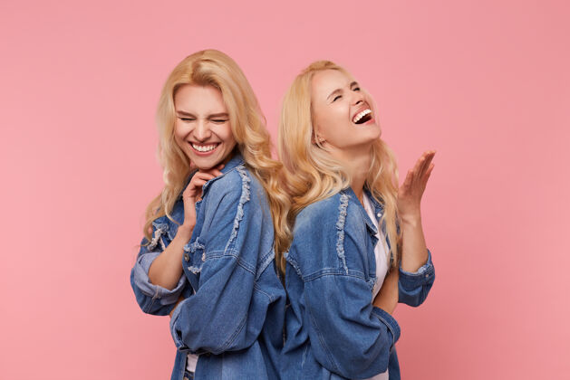 情绪快乐的年轻的长发金发的姐妹们在摄影棚的照片在高的精神和欢笑闭上眼睛 而站在粉红色的背景背部休闲姐妹