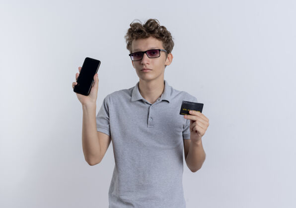 认真一个穿着灰色马球衫的年轻人站在白墙上 手里拿着信用卡 表情严肃马球脸移动