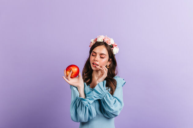 表情心情很好的女孩正看着美味的红苹果隔着墙的蓝色女衬衫的快照女人人欢呼