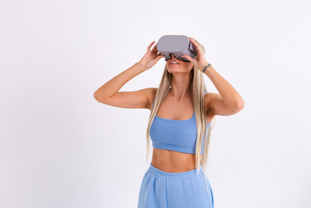 科技摄影棚照片中一个年轻迷人的女子穿着温暖的蓝色时尚西装 戴着虚拟现实眼镜在白色的视觉女性表情