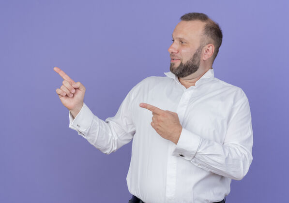 壁板一个留着胡子的男人穿着白衬衫 面带微笑 用食指指着站在蓝色墙上的一边胡子穿站