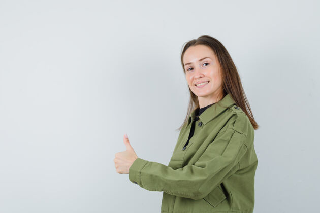 年轻穿绿色夹克的年轻女子竖起大拇指 看上去很积极微笑漂亮休闲
